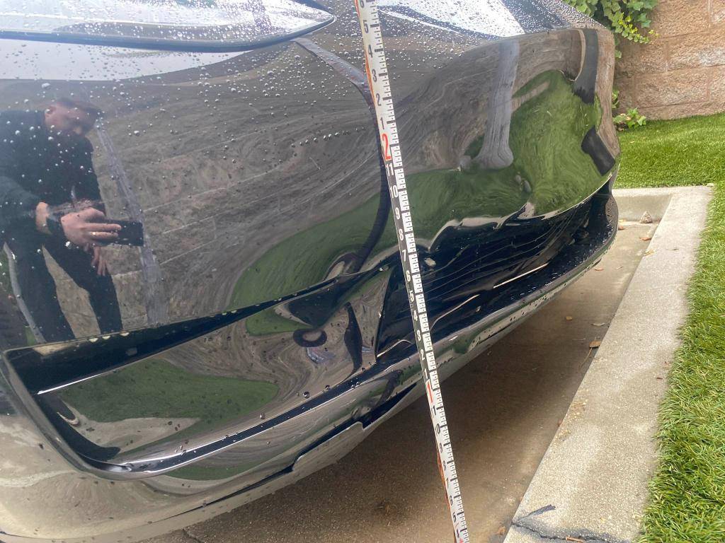 Tesla bumper repair damage documented with a measuring scale